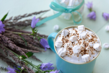 Delicious mocha with white marshmallows on an azure background with lilac flowers.