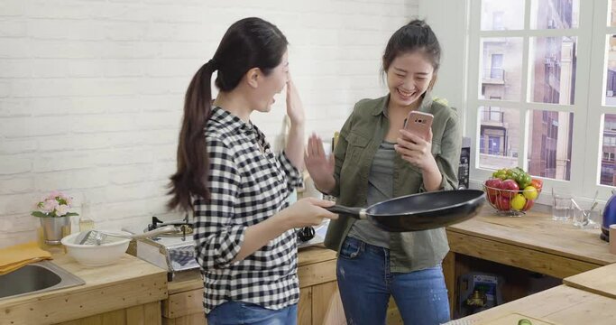 Happy family making handmade breakfast on weekend. two asian chinese sisters having fun in kitchen. happy young girl flipping pancake on pan and sibling recording video on cellphone share online