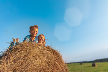 Naklejka na ściany i meble happy boy and girl on hay stack in wheat field