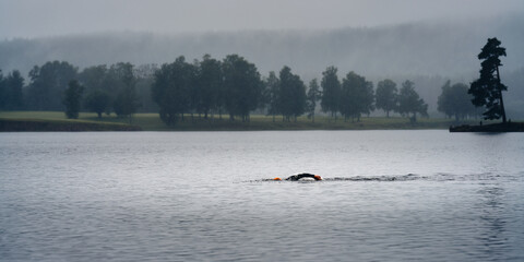 A unrecognizable man swims in a foggy lake a cold evening. Mist in the air. 