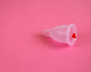silicone eco-friendly menstrual Cup in pink with a red heart symbolizing blood . pink background...