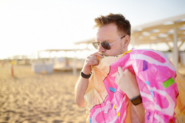 Man wearing sunglasses inflates an inflatable doughnut swimming circle on the seashore. Summer...