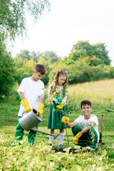 Two teenage boys and a girl of 8 years old in green clothes plant a tree in the garden