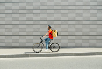 Fototapeta premium Delivery man on bicycle. Young guy with beard and big backpack rides along path in city
