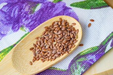 Flax seeds in a small wooden spoon lying on a colored linen towel. Nearby are fragments of a tree. In the daytime natural light