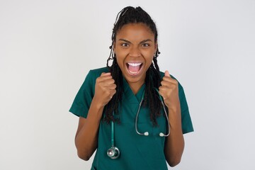 Caucasian young doctor woman rejoicing her success and victory clenching her fists with joy. Lucky woman being happy to achieve her aim and goals.