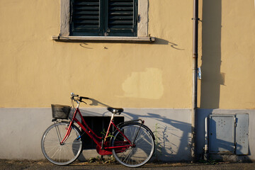 Fototapeta na wymiar A red bicycle leaning against a yellow wall with a green window
