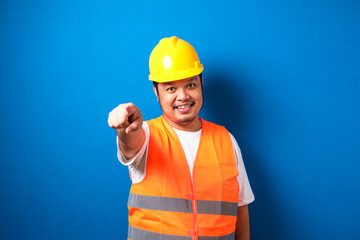 Young fat asian construction worker man wearing safety helmet pointing forward