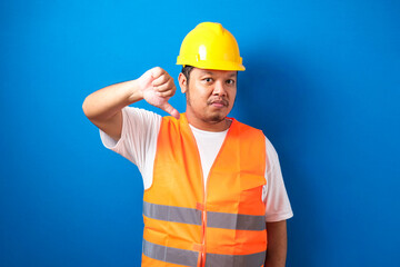 Young fat asian construction worker man wearing orange safety vest and helmet looking unhappy and...