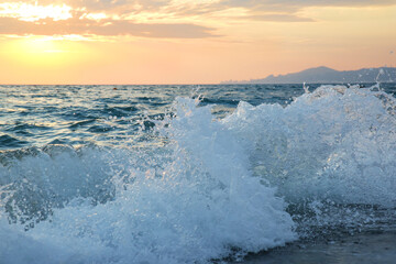 a wave breaks on the shore at sunset