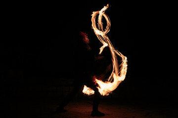Long exposure shot from a fire juggling act, performed by a man with a red hat, showing the light trail create by the 3 burning torches. 