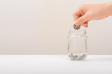 White hand man holding coin to putting in Jar or glass bottle for saving with soft white background. Saving money, Saving concept