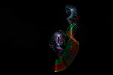 Long exposure shot, following the light trail from electrical juggling clubs that glow in changing colors, with the Juggler’s silhouette hidden between them.