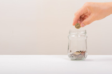 White hand man holding Gold coin to putting in Jar or glass bottle for saving with soft white background. Saving money, Saving concept