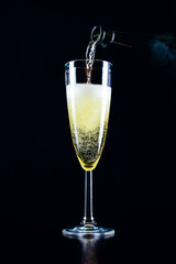 Sparkling wine pours from a bottle into a glass on a dark background