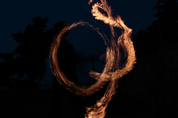 Long exposure shot from a fire juggling act, performed by a man with a red hat, showing the light trail create by the 3 burning torches.