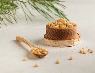 Pine nuts in a wooden bowl and in a wooden spoon on the background of a coniferous branch. Copy...