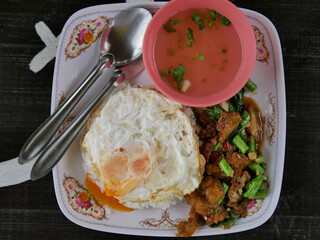 crispy pork belly basil stir fried with fried egg and soup on a wooden table,thai food.