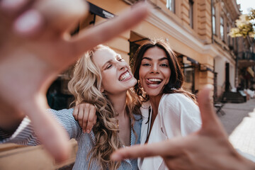 Appealing fair-haired woman fooling around with friend. Latin brunette girl spending time outdoor...