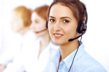 Call center operators. Focus on beautiful business woman using headset in sunny office