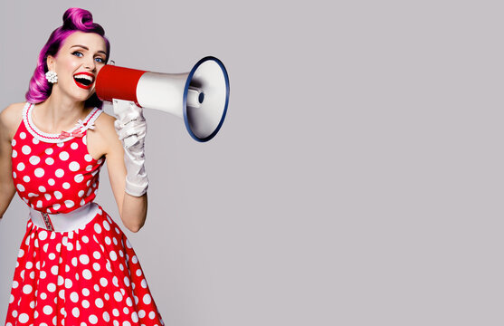 Purple head woman using megaphone, shouting something. Pin up girl in red polka dot dress. Retro vintage studio concept. Grey color background. Copy space place for some text.