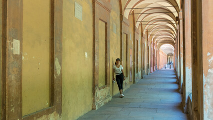 Asian woman in hat, tshirt and sneakers leaning against wall of portico © David