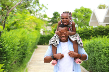 African American father gave piggyback ride to his little daughter and having a good time together while walking outside the house around the neighborhood - Powered by Adobe