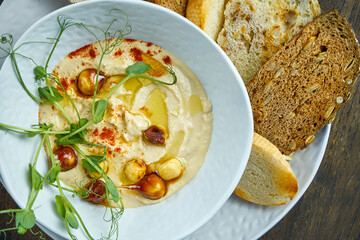 A classic oriental snack - chickpea hummus with caramelized peanuts and croutons in a white plate. Selective focus