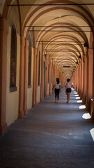 Mother and daughter walking through arched portico in a summer day