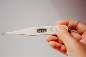 Disease and fever. First symptoms of the coronavirus. Electronic thermometer with a display value of 37.1 degrees in the hand of a woman on a light white background close-up with  place for text.