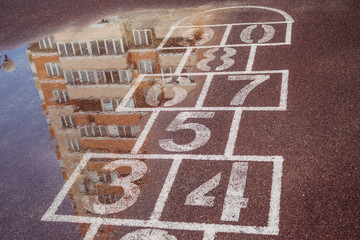 The concept of bad weather. Marking for popular children's games on the street in the yard on the sports surface after the rain with the reflection of a part of a multi-storey building in a puddle.