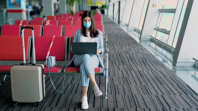 woman in protective mask, with luggage, working on laptop at airport, while waiting for boarding. air lines opening after coronavirus epidemic