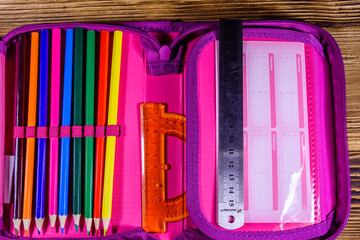Different school stationeries (pens, pencils, ruler and protractor) in a pink pencil box. Top view