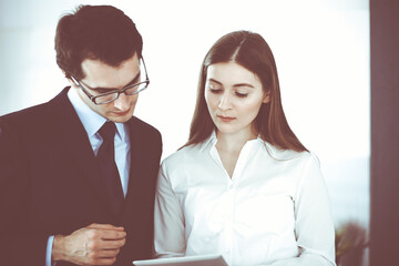 Businessmen and woman using tablet computer in modern office. Colleagues or company managers at workplace. Partners discussing contract. Business concept