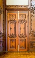 Closed elegant lumber door with engraved decorations, installed in wooden ornamental archway leading to old building