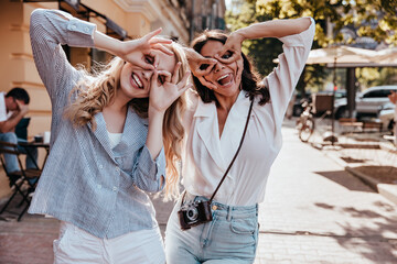 Amazing brunette woman in white blouse fooling around on the street. Outdoor shot of glad female friends.