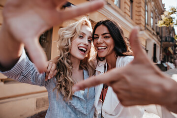 Laughing blithesome woman with dark hair walking down the street with friend. Carefree blonde girl...