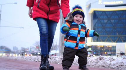 Mom and baby walk down the street in winter. A happy child is smiling at the camera. Slow motion