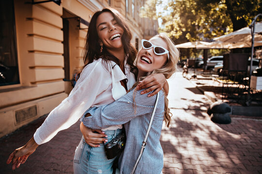 Glamorous woman in sunglasses embracing her sister. Outdoor photo of wonderful girls spending weekend together.