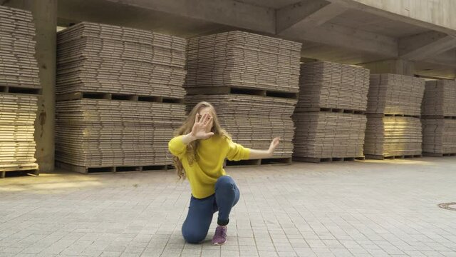 long shot 4K. modern choreography concept. A young plastic girl in a bright yellow sweater contemporary dancer is dancing on the street on an industrial background.