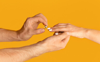 Young man putting engagement ring on his bride's finger over orange background, closeup