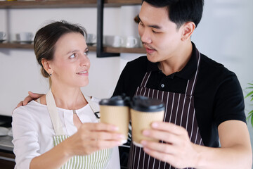 Smiling young barista couple loves Asian man and caucasian woman holding cups of hot coffee together. Start up Coffee shop and cafe business concept.
