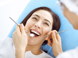 Smiling brunette woman being examined by dentist at dental clinic. Hands of a doctor holding dental instruments near patient's mouth. Healthy teeth and medicine concept