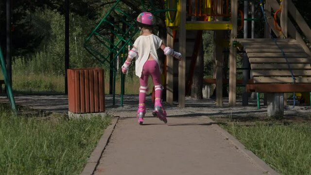 Cute Little Girl Wearing Protection Pads and Helmet Roller Skating near a Playground. Childhood, Summer Activities and Healthy Lifestyle Concept