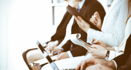 Business people working at meeting or conference, close-up of hands. Group of unknown businessmen and women in modern white office. Teamwork or coaching concept