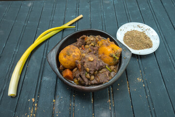 Stewed veal with potatoes, carrots and spices in a clay bowl on a black wooden base