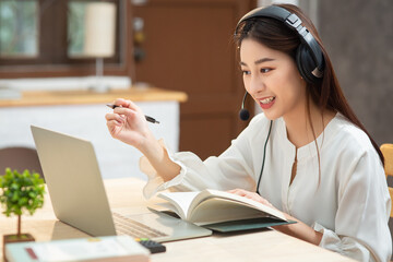 Smiling Asian young female using headset looking at laptop screen listen and learning online courses. Happy chinese business woman with headphones video call for customer service - obrazy, fototapety, plakaty