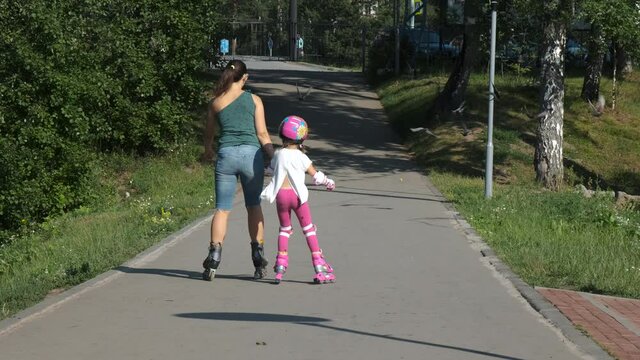 Little Girl with Mother Inline Skating Together Outdoors. Back Side View. Summer Family Activities and Healthy Lifestyle Concept
