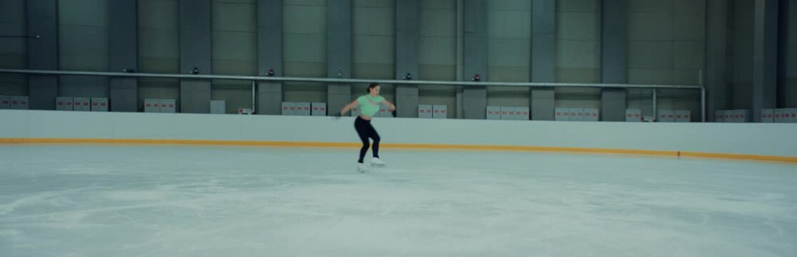 Professional teenager female ice figure skater practicing jumps on the rink. Shot on RED cinema camera with 2x Anamorphic lens, 75 FPS slow motion