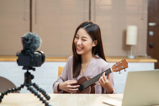 Asian teenage girl look at camera filming her self and playing ukulele guitar